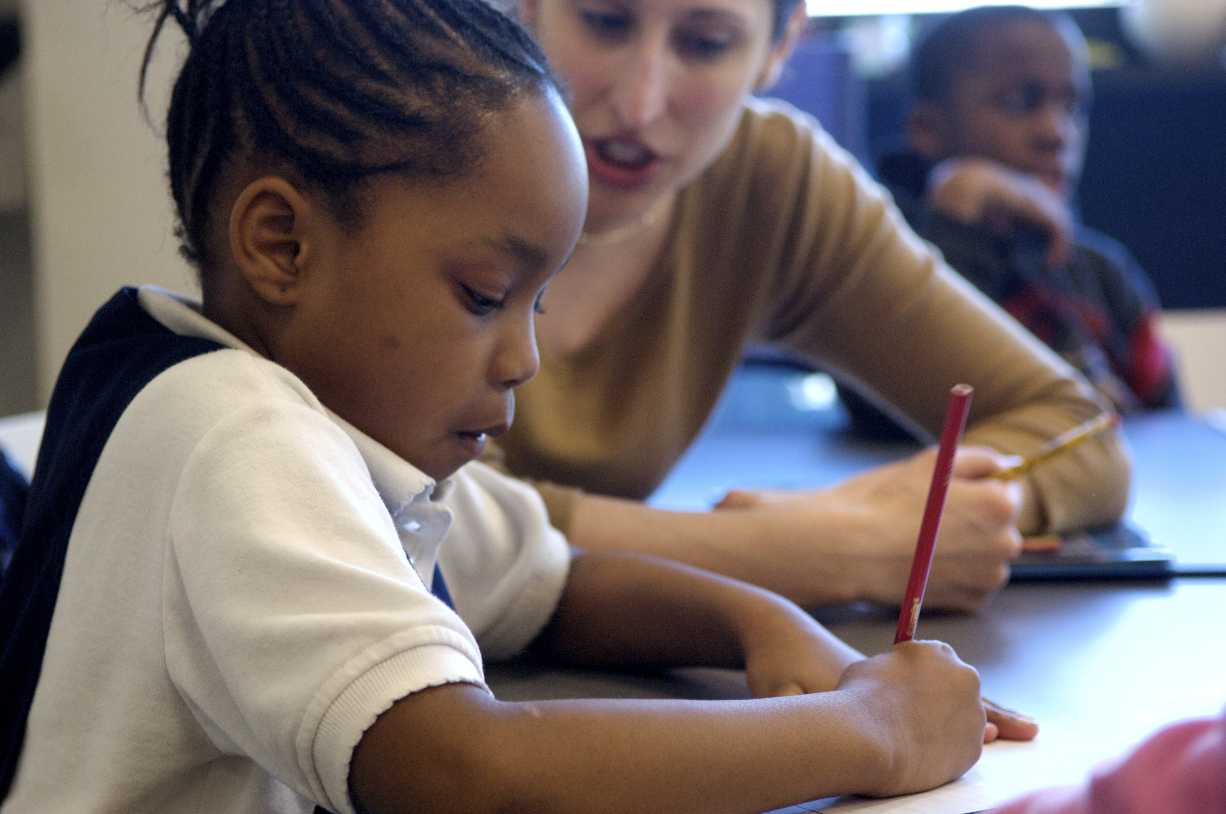 A woman helping a young girl with her writing.